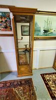 Full front view of tall curio cabinet showing wooden frame, mirrored back, glass shelves, and roll top molding.