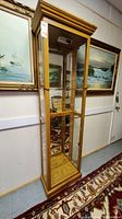 Full view of the tall curio cabinet showing its wooden frame, glass panels, and mirrored back with light fixture on top.