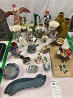 Full overview of multiple delicate porcelain figurines and vases including birds, a cat, and floral designs.