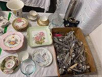 Overview showing assortment of china dessert plates, teacups, utensils, measuring glass, thermos, crystal decanter
