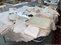 Overview photo of assorted embroidered linens on a table showing various pieces including napkins, tablecloths, doilies, and bureau scarves.