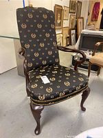 Front angled view of the laurel wreath patterned upholstered chair showing wooden armrests and cabriole legs.