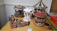 Four mechanized and musical carousel figurines arranged on a table, showing their relative sizes and details.