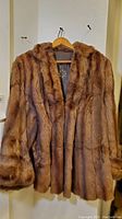 Full view of the brown vintage mink fur coat hanging on a wooden hanger, showing the coat’s length and fur texture.