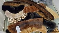 Photo showing multiple vintage fur collars laid out, including dark brown mink, black and brown fox fur, a spotted faux fur collar, and lighter rabbit fur collars.