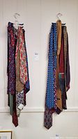 Two sets of men's neck ties hanging on black metal hooks on wall with a total of about 15 ties between two hooks. Various colorful patterns visible.
