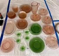 Full overview of multiple pink and green mid century glassware pieces including plates, bowls, covered dishes, and stemware on white background.