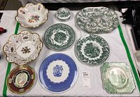 Full view of all nine plates and serving ware pieces arranged on a cloth, showcasing different patterns and shapes.