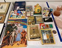 Wide view showing the full assortment of vintage pop culture items on a white cloth, including Wizard of Oz book, music and comic books, pins, card games, and small toys