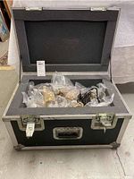Opened black vintage trunk filled with plastic bags of assorted costume jewelry inside foam insert.