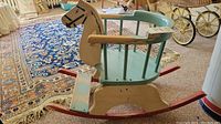 Side view of the antique child's rocking horse chair showing the horse head and spindle backrest, with visible signs of paint wear.
