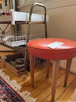 Side angle of cart and orange cushioned stool showing metal frame, wood shelves and stool legs