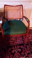 Front view of wood framed chair with green fabric seat placed on a patterned rug