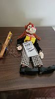 Full view of the wooden clown marionette puppet lying on a table with attached wooden control bar and tangled strings.