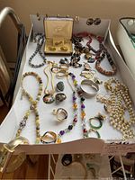 Photo showing assorted costume jewelry including necklaces, earrings, cuff links, bracelets, and a watch spread in a box