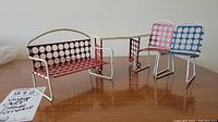 Photo showing the vintage metal doll house furniture set including two chairs, bench, and table on a wooden surface.