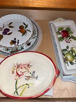 Overview of assorted porcelain plates and platters, highlighting the oval hummingbird platter, covered rectangular dish and stacked fruit motif plates.