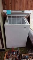 Full view of white Woods chest freezer with the lid open showing the interior basket and external condition.