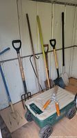 Photo showing garden tools leaning against a wall and the garden cart stool on the floor with shears on top.