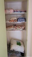 Wide shot of linen closet shelves filled with folded linens including comforters, blankets, and sheet sets.