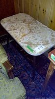 Photo of the entire mid-century modern table showing the beige marble or marble-like top with natural veining, positioned near a green chair and wooden paneled wall.
