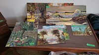 Multiple landscape art pieces on table including Robert Wood prints and amateur garden painting