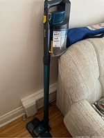 Full vacuum cleaner upright near wall and couch, showing the complete unit.