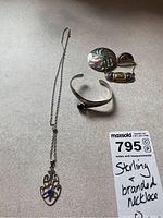 Photo of sterling silver necklace with detailed silver pendant and chain, sterling cuff bracelet with black stone, and three brooches including a round shell inlay brooch and an oval striped brooch.
