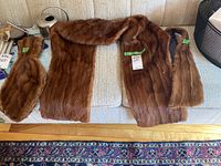 Studio photo of three brown fur stoles laid out flat on a light beige couch showing full length and color.