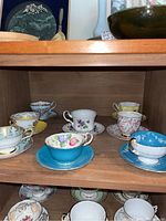Six cups and saucers displayed on wooden shelf, front and center grouping
