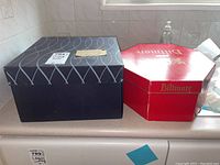 Two hat boxes side by side on kitchen counter; one Biltmore red octagonal box and one black patterned square box.