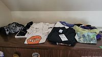 Photo showing folded vintage t-shirts including Milwaukee Brewers, A&W, Toronto Sun, Blue Jays and Pop Shoppe logos in various colors and styles.