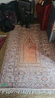 Full view of the hand knotted wool rug showing fringe detail and design pattern with adjacent luggage for scale.