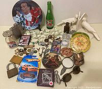 Wide view of assortment of vintage collectibles including sports plate, glass bank, flask, coins and tokens, decorative plates, and novelty items