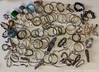Wide view of multiple bracelets and bangles laid flat on a light surface showing variety in style and finish