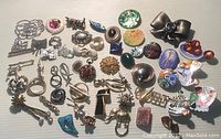 Over 50 assorted brooches lying on a surface, including silver-tone metal, ceramic, enamel, and rhinestone decorated pieces in various shapes including bows, leaves, flowers, and animals.