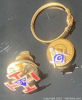 Two Masonic pins and child's ring grouped on a black surface.