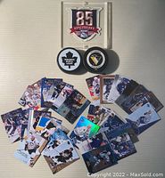 Top-down view of entire hockey memorabilia collection arranged on a flat surface including cards, two NHL pucks, and New York Rangers 85th Anniversary crest in clear display case.