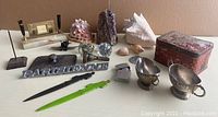 Wide view of various vintage items including perpetual calendar, seashells, metal sign, pens, glass doorknobs, decorative stone and metal items, and red box.