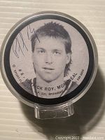Close-up photo of the hockey puck top surface showing a black and white portrait of Patrick Roy with autograph on top.