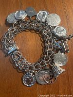 Full view of the silver charm bracelet showing chain and multiple coin and shaped charms.