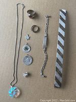 Full view of the sterling silver jewellery lot on a beige surface showing chain with pendant, two rings, three pendants, two bracelets, and a Mason pin
