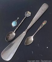 Top view showing all four items: spoon with emblem, shoehorn with monogram, floral decorated spoon, and grape cluster pendant.