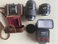 Photo of Kodak Retina Compur Rapid camera in leather case, two Minolta lenses, and Cobra electronic flash on a light surface, showing all items together.