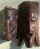 Two wooden masks side by side showing different carving styles and wood finishes under natural light.