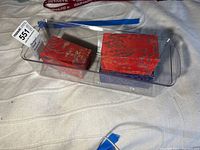 Three sets of Asian hand exercisers in clear plastic container on white cloth background.