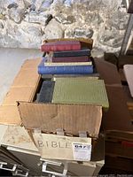 Photo of an open box filled with several Bibles of different colors and sizes stacked inside, showing the top row clearly.