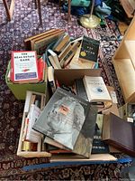 Books arranged in boxes and a basket on a carpeted floor showing multiple titles including real estate and historical subjects.
