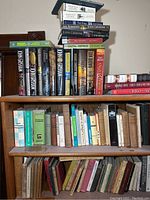 Three shelves of books, showing various titles including John Grisham and Dan Brown novels, Sherlock Holmes books, and assorted history and novel titles in hardcover and paperback.