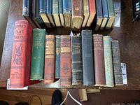 Top view of 14 vintage and hardback books with varied colors including red, green, and brown, titles visible on some spines